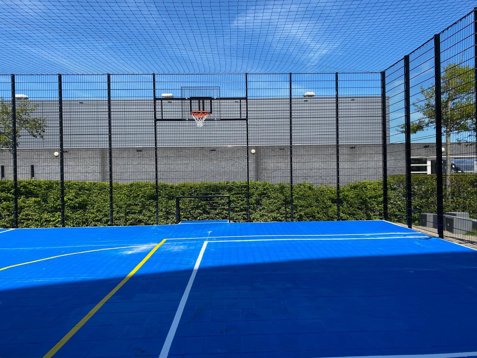 Sportvloercoating 25 Voetbalkooi met een blauwe Granuplast-coating met voetbal en basketbalbelijningen.